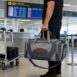 Homem em aeroporto segurando bolsa de passeio cinza ao lado do corpo