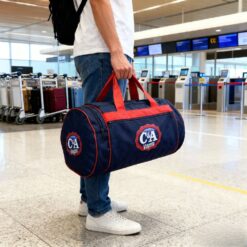 Homem em aeroporto segurando bolsa de viagem redonda na mão.