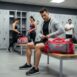 Homem sentado em banco de academiaao lado de sua bolsa esportiva cinza e vermelha