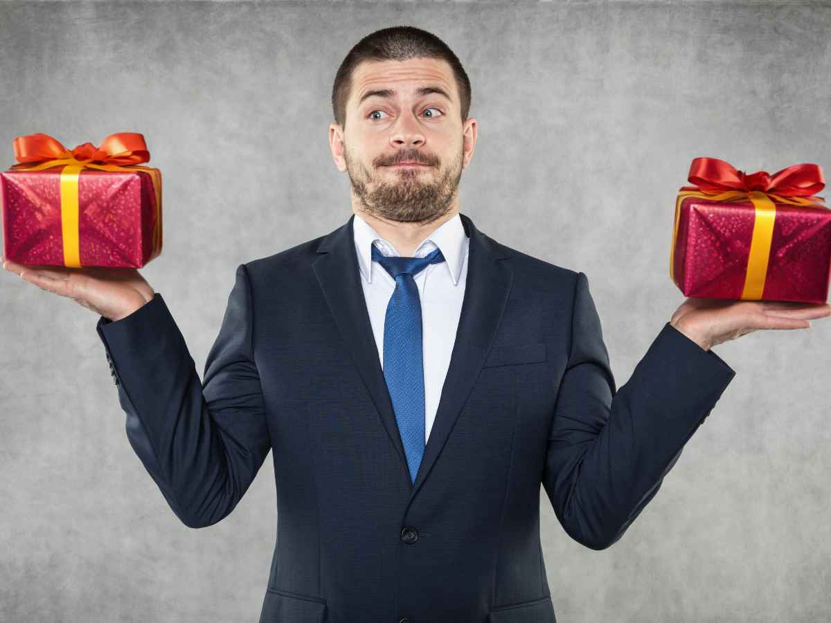 Dono de empresa em momento de decisão, segurando um brinde em cada mão na altura dos ombros e com expressão pensativa, refletindo sobre qual opção é mais adequada para presentear colaboradores e clientes, preocupado em não cometer erros na escolha e garantir que o brinde represente bem a imagem da empresa.