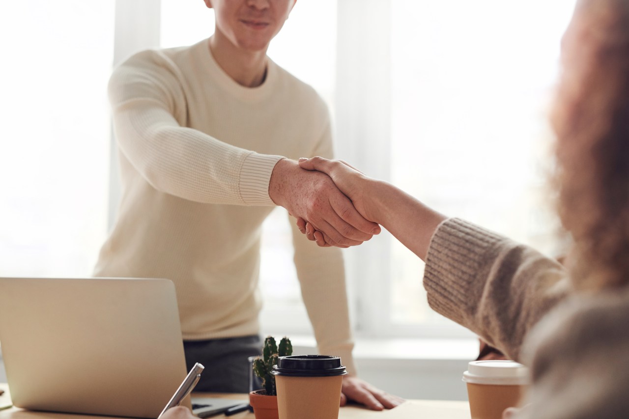 Dona de empresa recebendo novo funcionário com um aperto de mão.