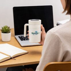 Mulher segurando caneca térmica branca em frente a um notebook