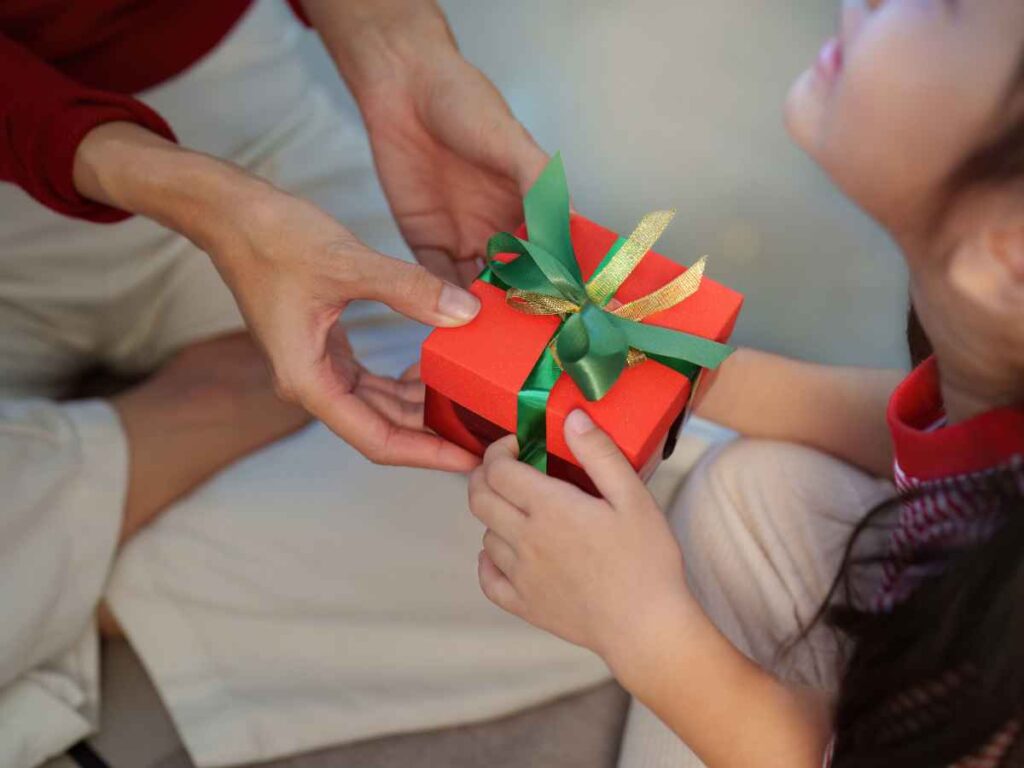 Criança recebe uma caixa de presente das mãos de um adulto