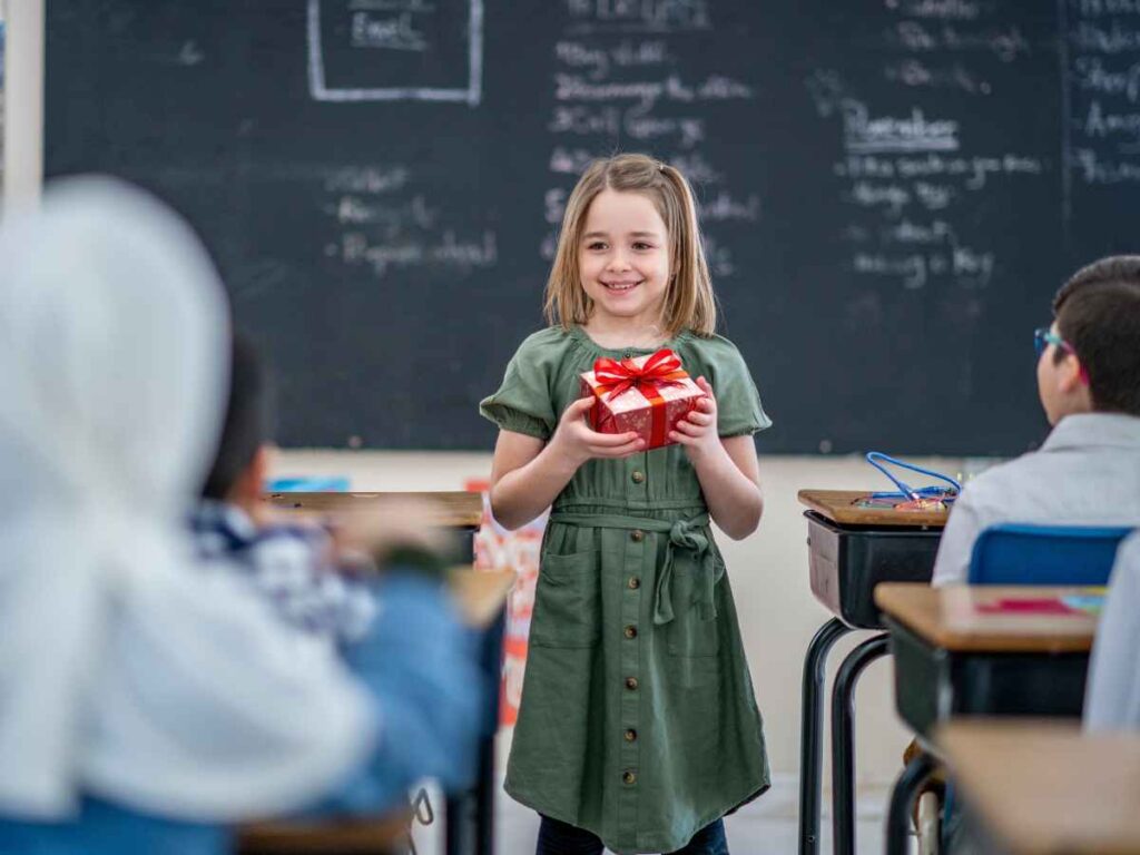 Criança em sala de aula segura um presente enquanto colegas observam
