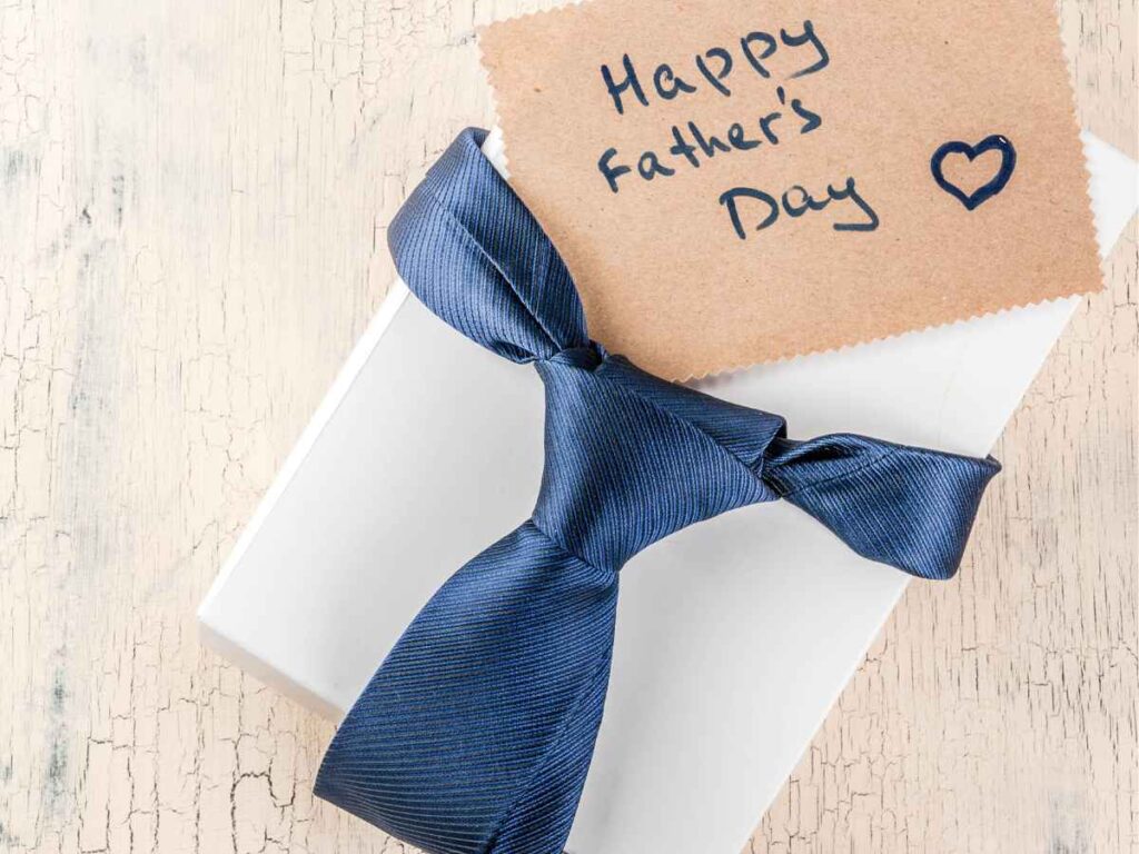 Caixa de brinde branca amarrada com uma gravata azul marinho e cartão escrito “Happy Father’s Day” ao lado.
