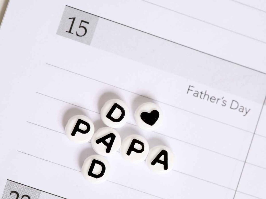 Página de calendário marcando o Dia dos Pais no dia 15, com letras decorativas formando a palavra "PAPAI" e um coração.