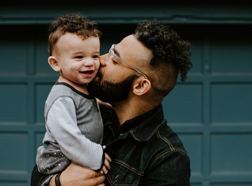 Pai com jaqueta jeans beijando um bebê menino que segura no colo. 