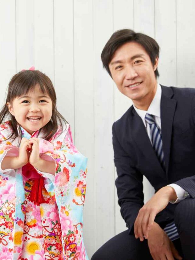 Família sorridente, com uma criança vestida em traje colorido, posando ao lado dos pais em um ambiente iluminado. A cena transmite alegria e união, representando a comemoração do Dia das Crianças em empresas.