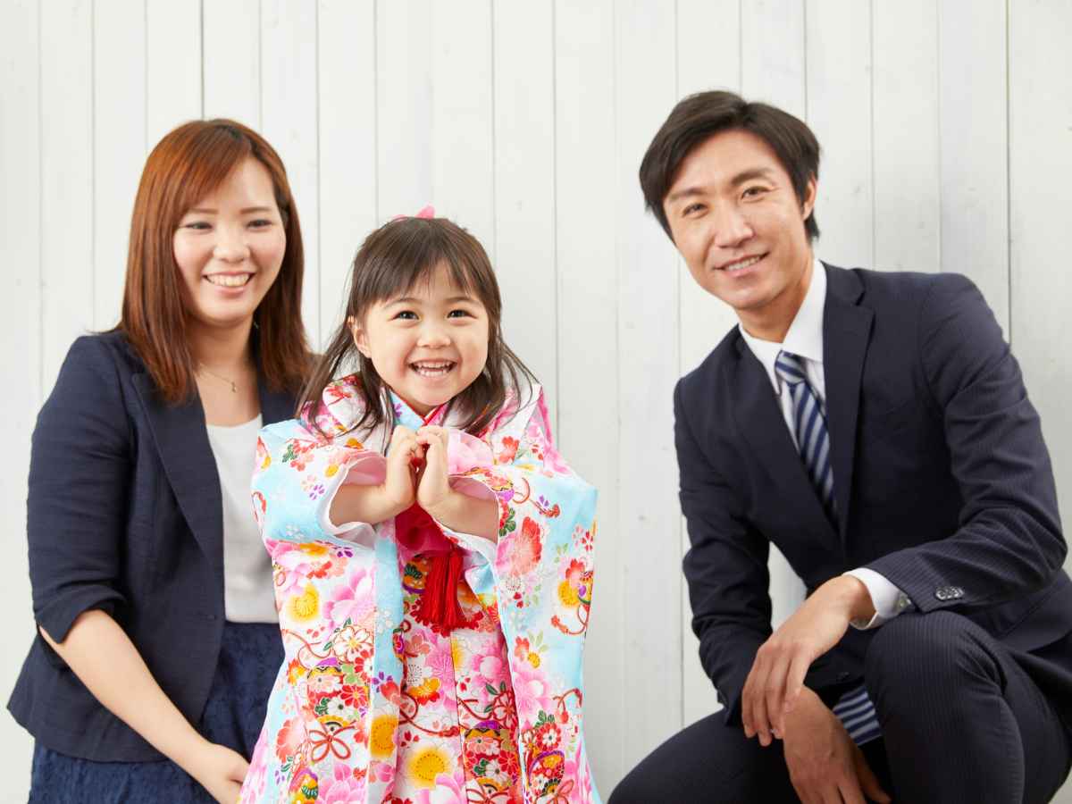 Família sorridente, com uma criança vestida em traje colorido, posando ao lado dos pais em um ambiente iluminado. A cena transmite alegria e união, representando a comemoração do Dia das Crianças em empresas.