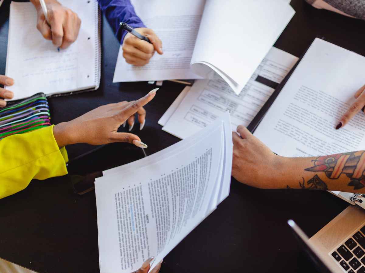 Colaboradores de uma empresa reunidos em torno de uma mesa repleta de papéis, estudando e se desenvolvendo profissionalmente.