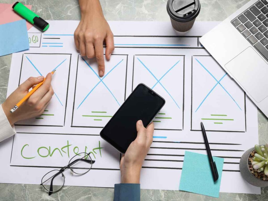 Equipe trabalhando na criação do esboço de um site em papel, planejando sua implementação para torná-lo otimizado e responsivo, com o objetivo de melhorar a visibilidade corporativa.