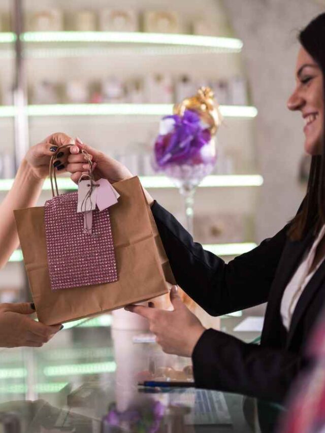 Mulher de blusa branca com botões presenteando sua cliente vip que utiliza um blazer.