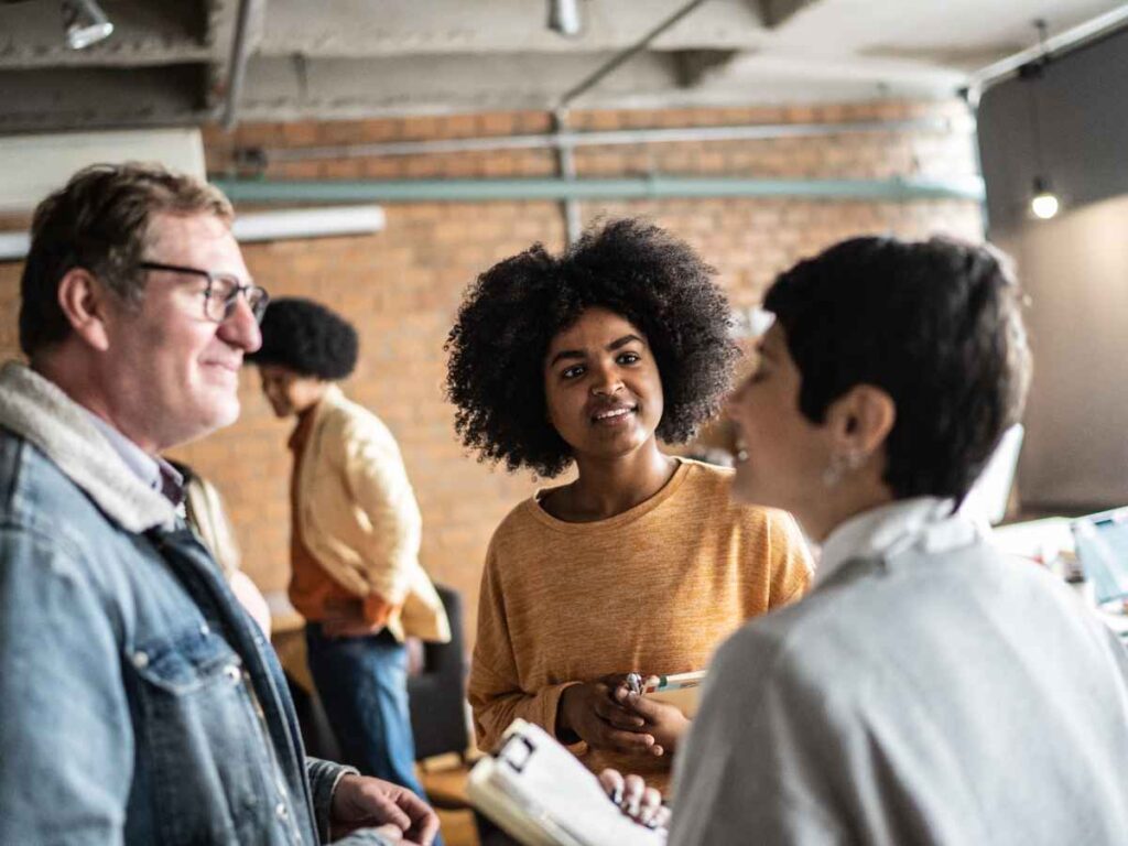 Dona de empresa conversando com dois possíveis clientes. Enquanto toma nota da conversa.