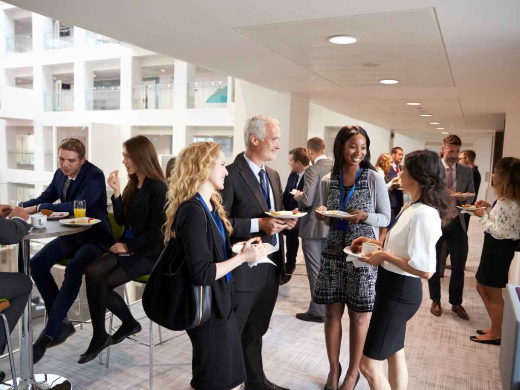 Empresa organizando um evento corporativo interno para integrar seus funcionários. Os participantes do evento estão centralizados na imagem, comendo e conversando.