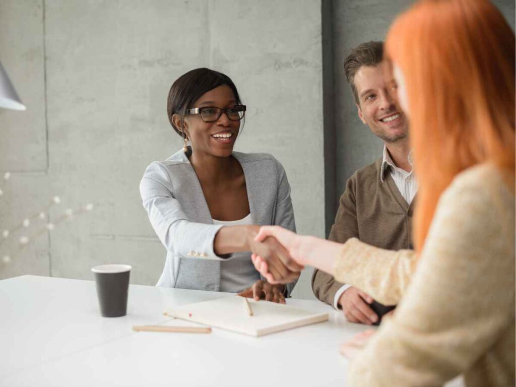 Dona de empresa fechando negócio com uma fabricante de brindes personalizados bem recomendada. As duas empresárias apertam as mãos em sinal de acordo e parceria, celebrando a escolha de um fornecedor confiável para fortalecer as ações promocionais da marca.