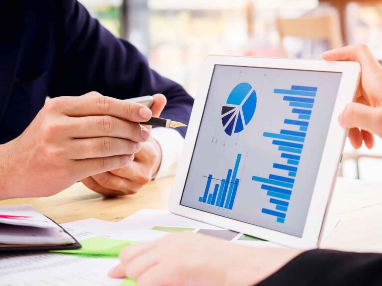 Dois colaboradores analisam um gráfico exibido na tela de um tablet, que ilustra o impacto de diferentes estratégias no aumento da visibilidade da empresa. Eles observam atentamente os dados, avaliando o crescimento projetado para cada abordagem.