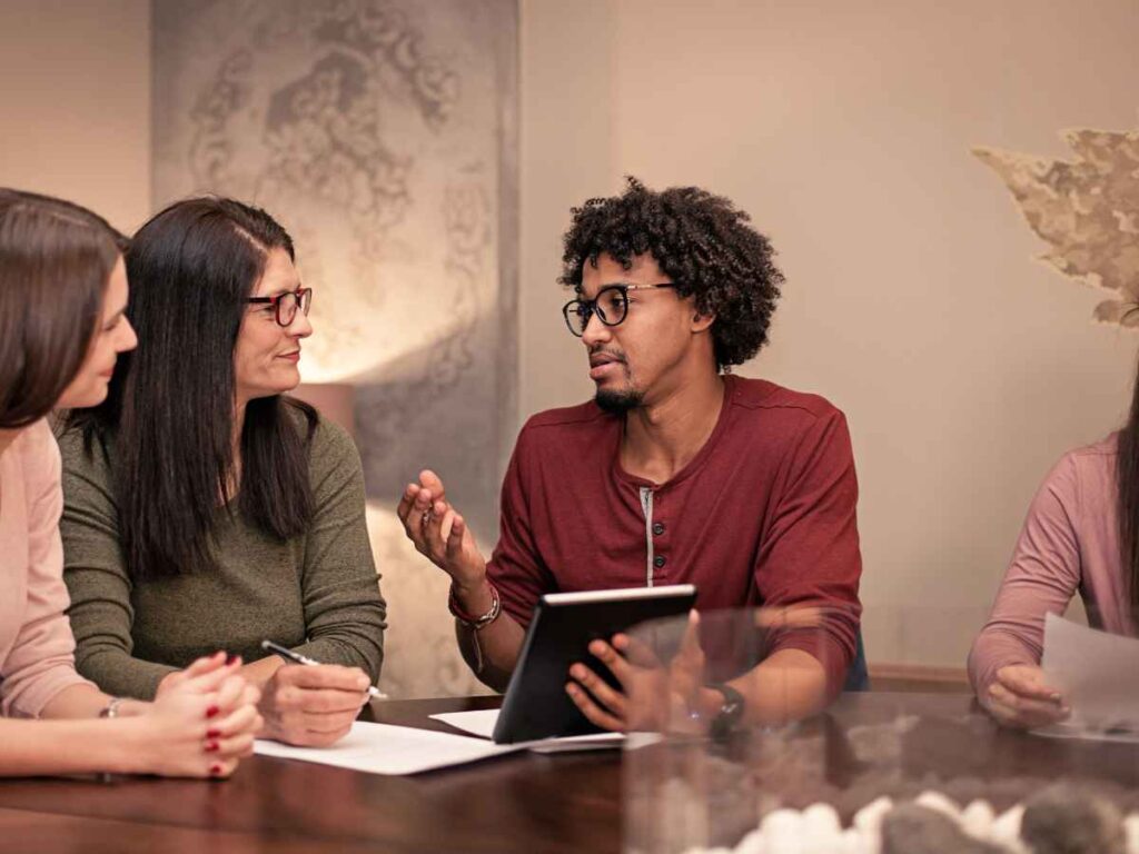 Grupo de trabalhadores de uma empresa reunidos em mesa de planejamento, discutindo a importância de os brindes refletirem os valores e a identidade da organização. Juntos, eles elaboram uma campanha de distribuição de brindes voltada aos funcionários, buscando alinhamento com a cultura corporativa e valorização interna.