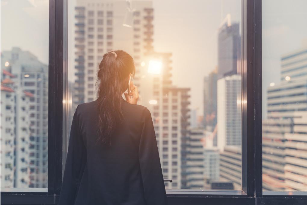 mulher de terno trabalhadora olhando o sol entre prédios no horizonte pelo vidro da janela