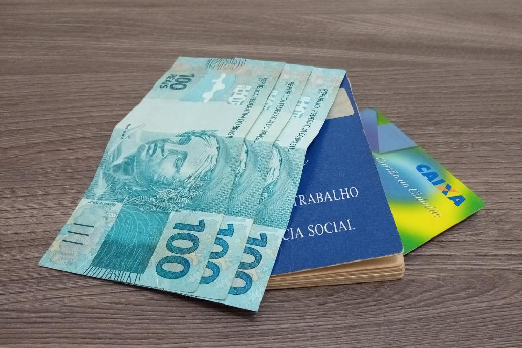 notas de cem com carteira de trabalho em mesa