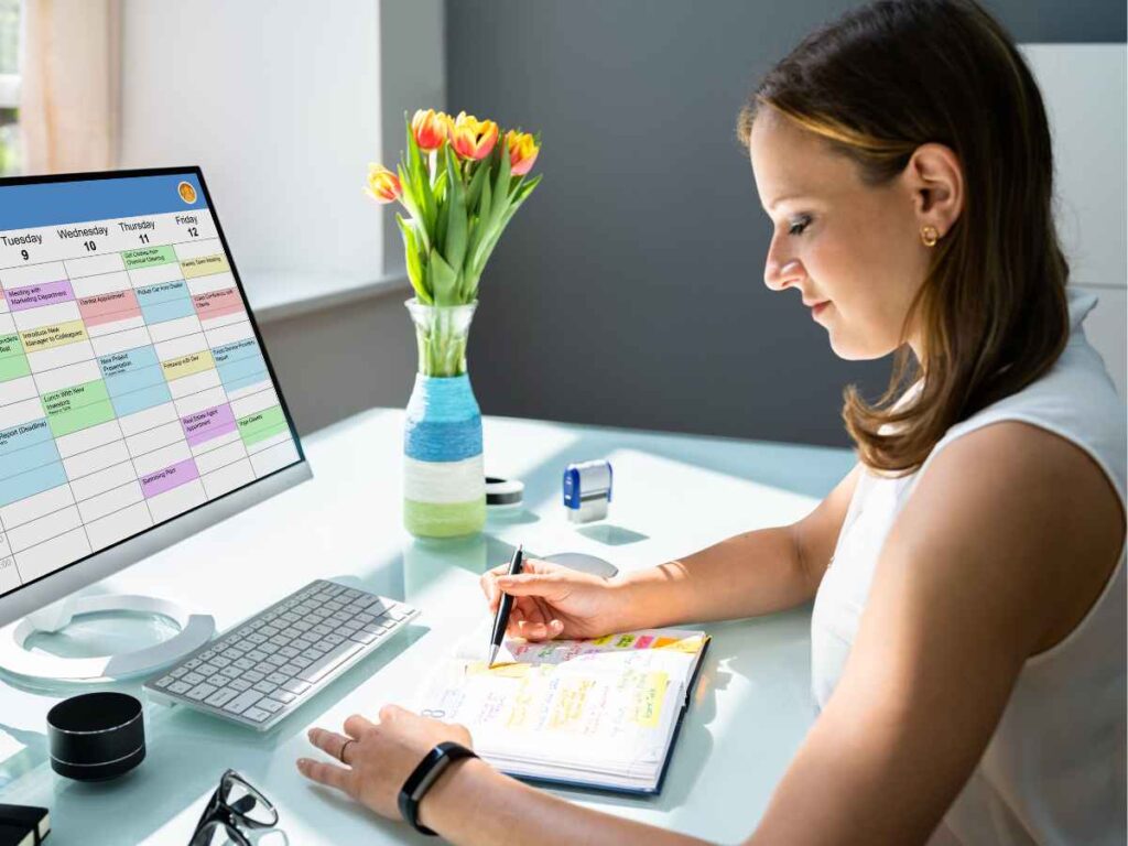 Dona de empresa organizando o cronograma de compra de brindes para evitar imprevistos. Sentada em frente ao computador com um calendário aberto na tela, ela faz anotações em um caderno, planejando datas estratégicas para garantir uma entrega eficiente e alinhada às ações da empresa.