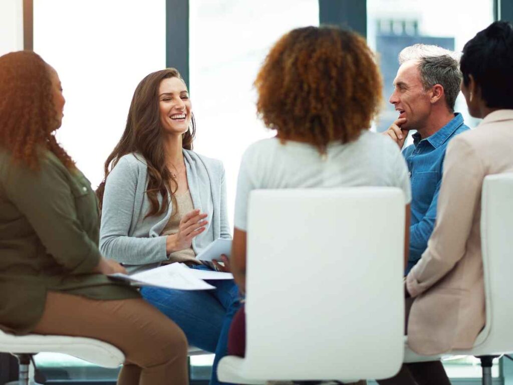 Cinco integrantes de uma equipe corporativa reunidos em roda, sorrindo e demonstrando felicidade por estarem juntos. O momento reflete a harmonia e o clima organizacional positivo da empresa, promovendo união e bem-estar entre os colaboradores.