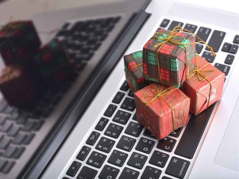 Pequenas caixas de presente decoradas com laços dourados sobre o teclado de um notebook.