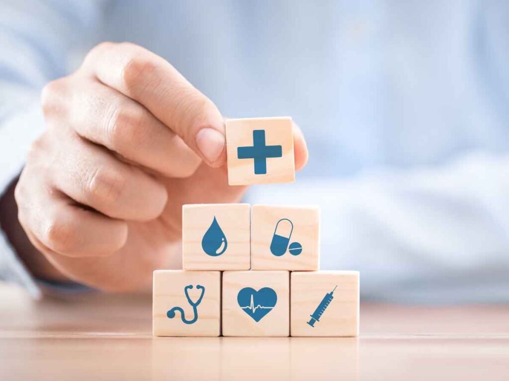 Mão posicionando bloco com símbolo de saúde sobre outros blocos com ícones médicos, representando a importância do SESMT na promoção da saúde e segurança no ambiente corporativo.