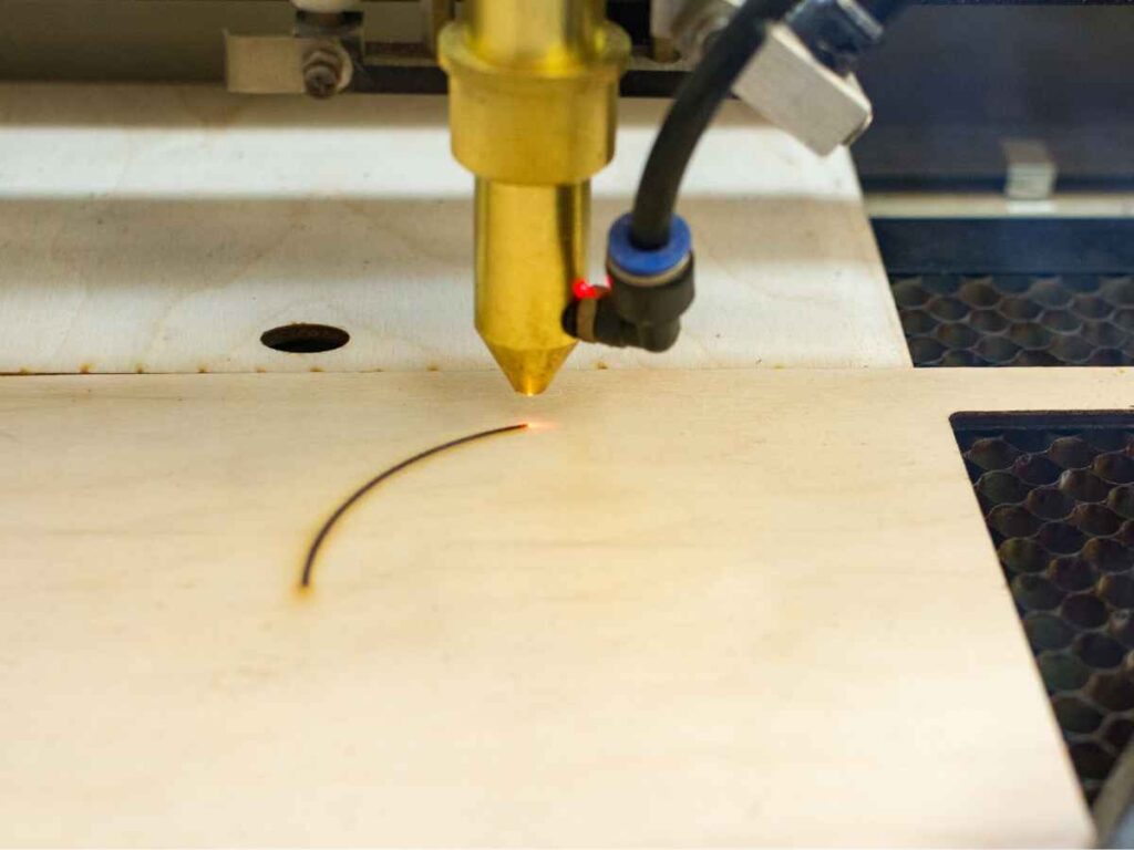 Máquina de gravação a laser realizando corte preciso em peça de madeira clara, evidenciando a técnica de personalização por meio de feixe de luz para criar detalhes finos e duradouros.