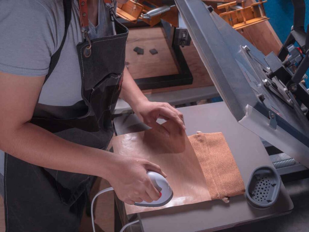 Profissional aplicando técnica de sublimação em toalha de tecido bege com uso de prensa térmica.