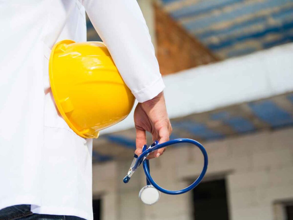 Profissional de saúde ocupacional segurando um estetoscópio e um capacete de segurança em um ambiente de obra, simbolizando a integração entre saúde e segurança no trabalho.