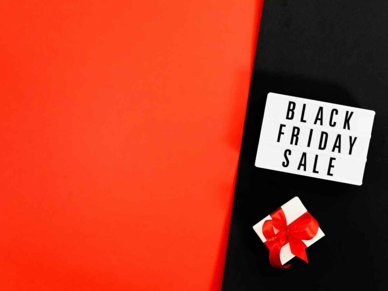 Fundo nas cores preta e vermelha com placa escrita “Black Friday Sale” e brinde embrulhado com laço vermelho