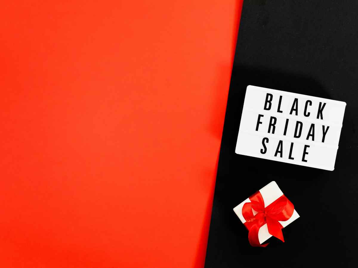 Fundo nas cores preta e vermelha com placa escrita “Black Friday Sale” e brinde embrulhado com laço vermelho