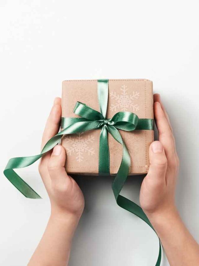 Mãos segurando uma caixa de presente embrulhada em papel kraft com laço verde brilhante, vista de cima