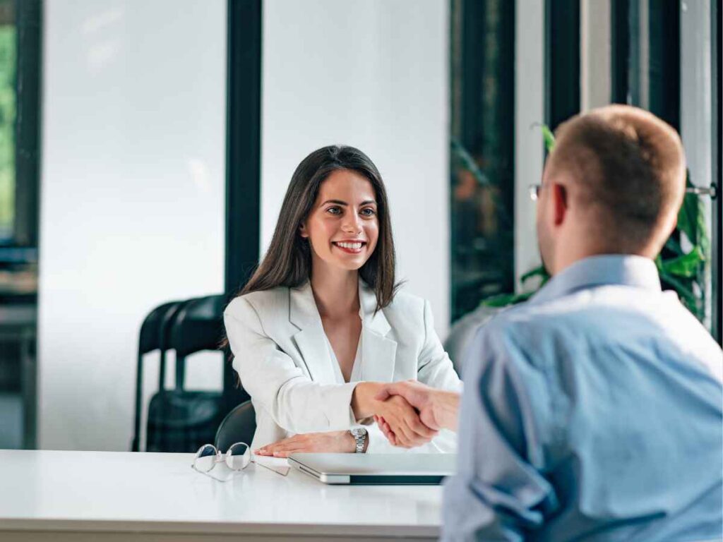 Mulher em ambiente corporativo apertando a mão de um homem durante reunião profissional em escritório moderno.