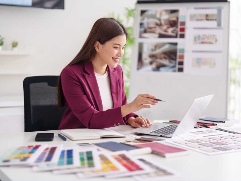 Profissional analisando e aprovando projeto de design em notebook com amostras de cores e materiais sobre a mesa.
