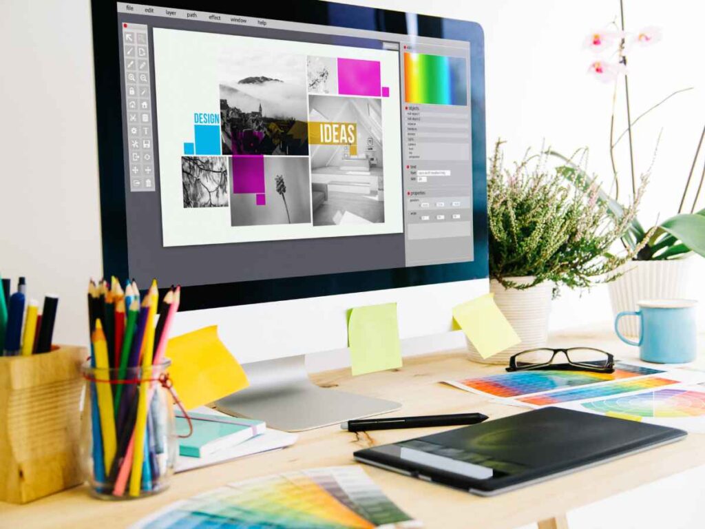 Monitor exibindo arte de projeto de identidade visual em mesa de trabalho com materiais criativos.