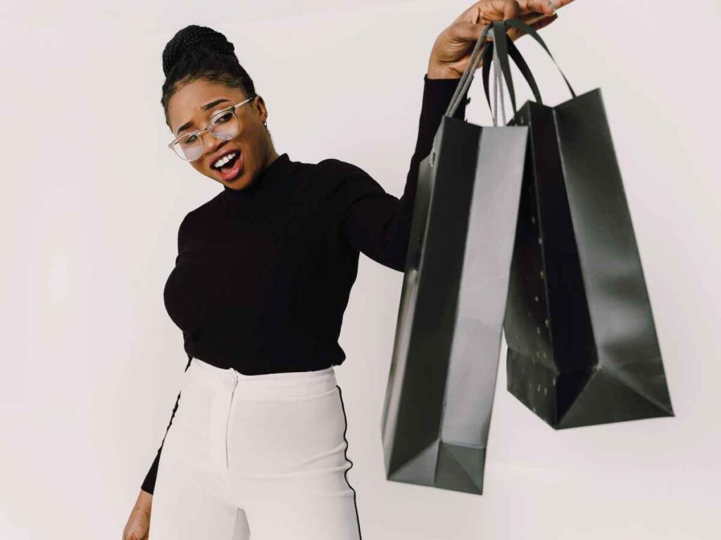 Mulher sorrindo e segurando várias sacolas de brindes em fundo claro