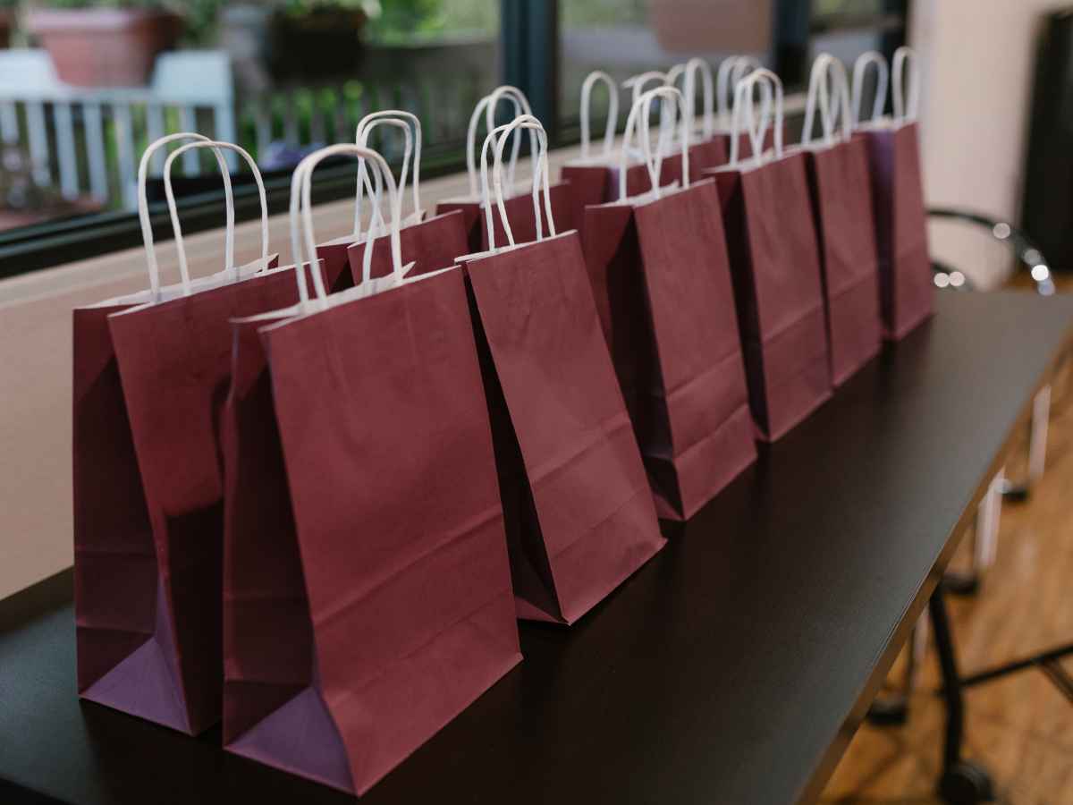 Sacolas de papel vermelho alinhadas sobre mesa, preparadas para distribuição de brindes em evento de lançamento imobiliário.